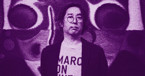 A person with glasses stands in front of a psychedelic, circular, purple-toned background. The lighting and patterns create a surreal effect, and text on their shirt is partially visible. © Illustration by ArtCritic.