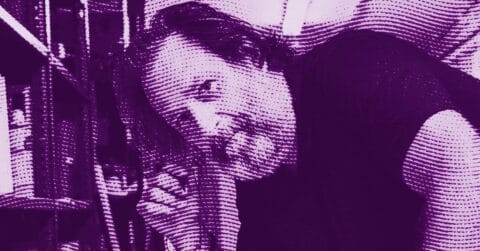 A man with medium-length hair and a beard leans forward, partially obscured, looking at the camera. The image is in a purple duotone with a halftone pattern effect. Shelves are visible in the background. © Illustration by ArtCritic.