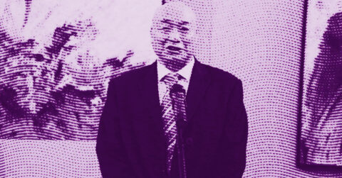 A man in a suit and tie stands indoors, with a plant and a framed picture in the background. The image has a purple halftone effect, giving it a stylized, textured appearance. © Illustration by ArtCritic.