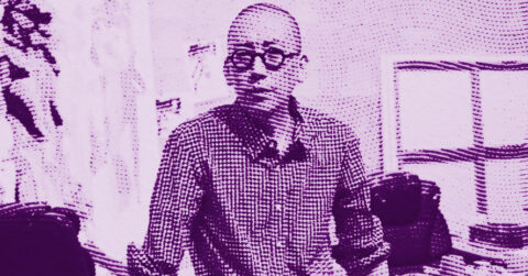 A pixelated, purple-tinted image of a person wearing glasses and a checkered shirt, standing indoors with shelves and objects in the background. The dotted filter effect obscures facial details. © Illustration by ArtCritic.