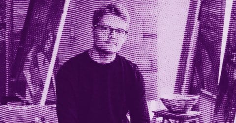 Alfie Caine wearing glasses sits indoors in front of curtains. The image has a purple tint with a wavy, textured filter effect applied, creating a stylized and abstract appearance. © Illustration by Art Critic.