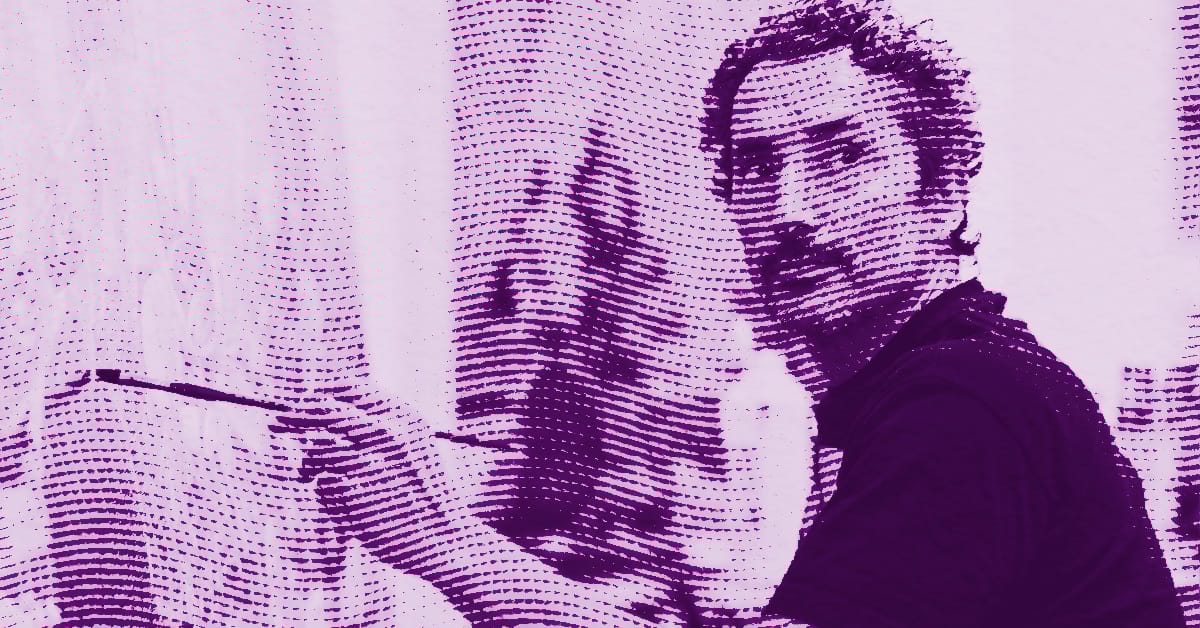 Kent Monkman with short hair and a mustache looks toward the camera while holding a paintbrush near a canvas. The image has a purple halftone effect, giving it a stylized, artistic appearance. © Illustration by Art Critic.
