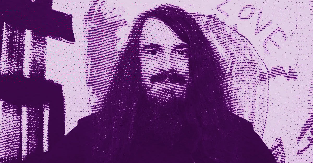 Jonathan Meese with long hair and a beard smiles in front of a wall with graffiti-style writing. The image is edited in a purple halftone effect, giving it a pop-art appearance. © Illustration by Art Critic.