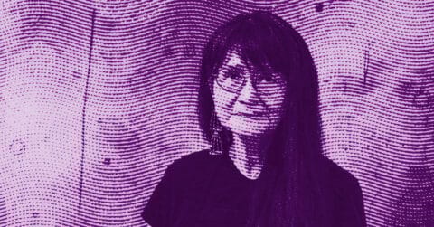A stylized purple halftone image of Emmi Whitehorse with long hair and glasses, smiling, standing against a textured wall with wavy lines. © Illustration by Art Critic.