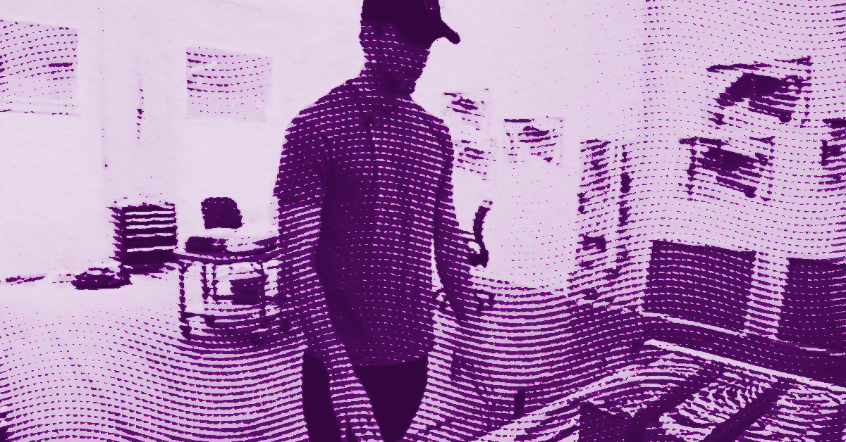 Kelley Walker in a cap stands in a room with shelves and various objects; the image has a purple filter and a wavy, dotted effect that partially obscures details. © Illustration by Art Critic.