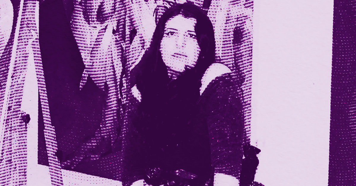 A stylized, purple-tinted image of Ilana Savdie with long dark hair sitting and looking slightly upward, surrounded by a blurred, dotted background with other indistinct figures. © Illustration by Art Critic.