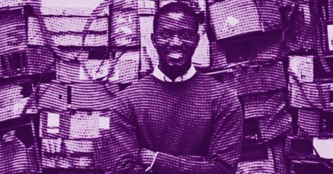 Ibrahim Mahama standing with arms crossed and smiling, in front of a background filled with many stacked bags. The image is filtered in purple tones. © Illustration by Art Critic.